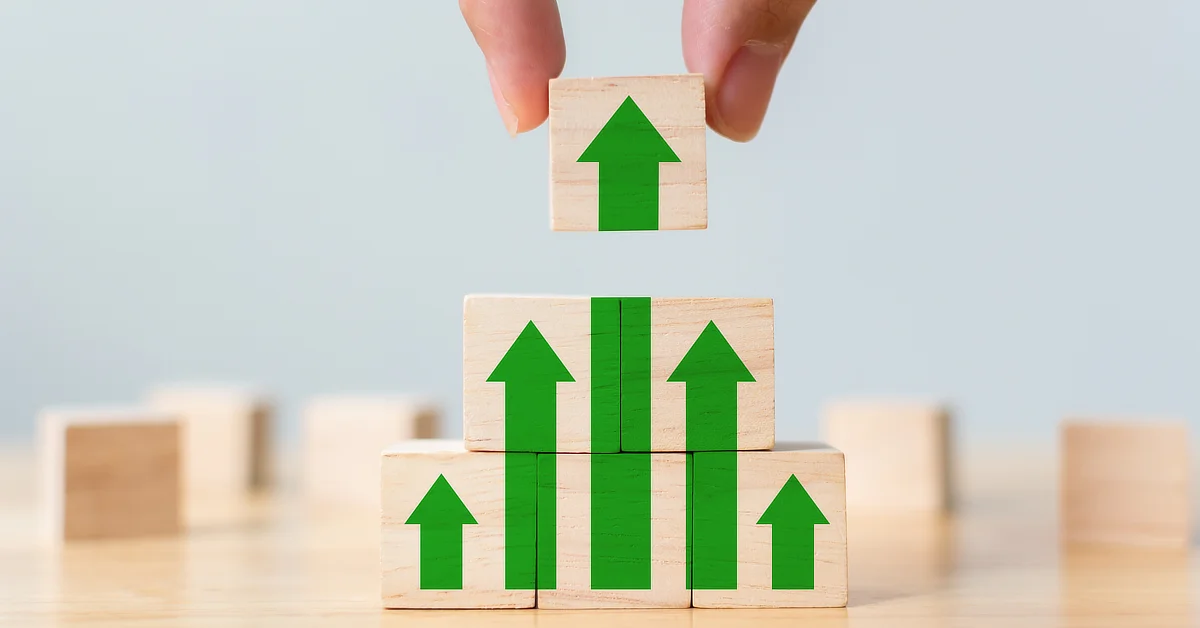 Hand stacking wooden blocks with green arrows pointing upwards.