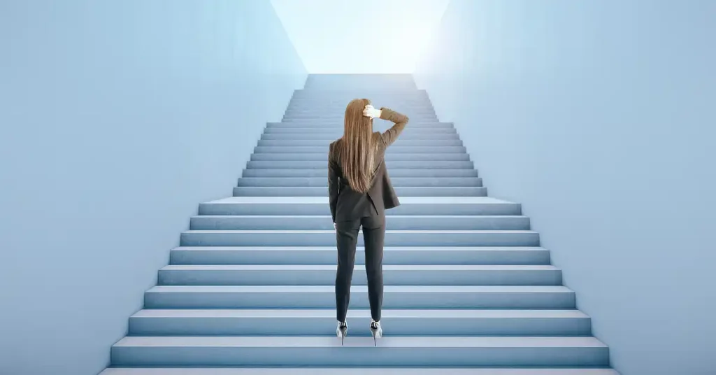 Person in a suit standing at the bottom of a wide staircase, looking up towards the top.