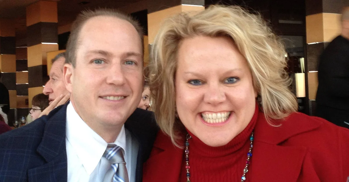 Kim Woods with her husband smiling at the camera during an outdoor event.