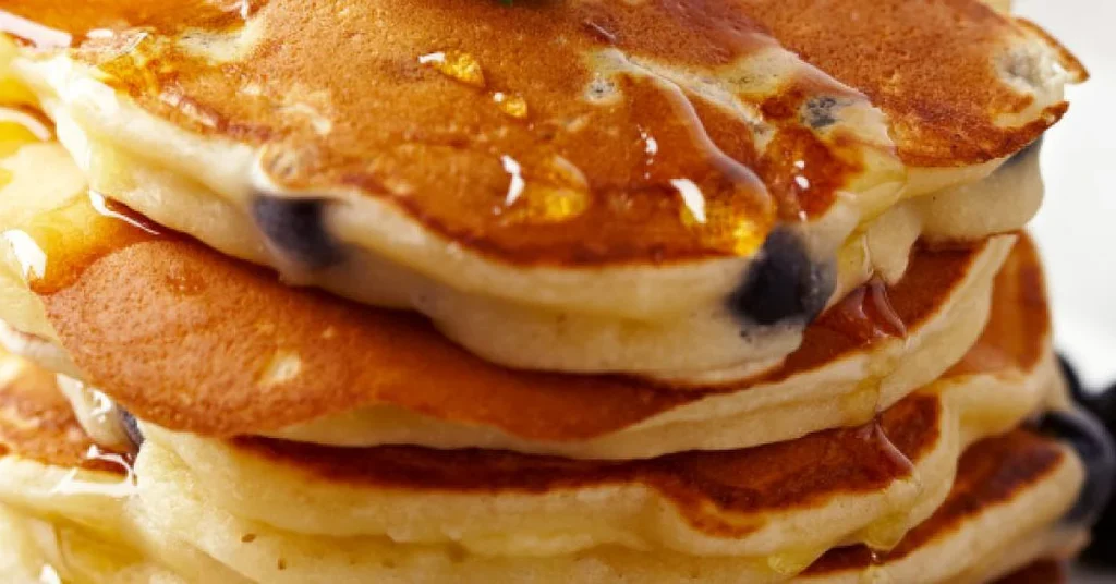 Close-up of a stack of blueberry pancakes drizzled with syrup.