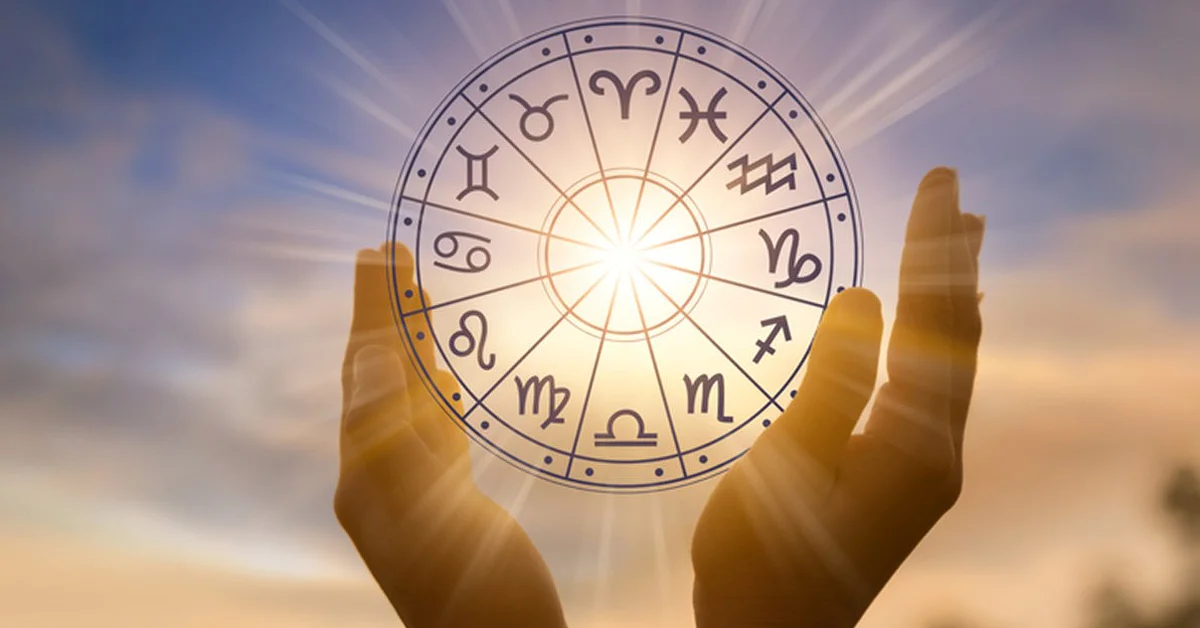 Two hands holding a glowing zodiac wheel with astrological symbols, set against a sunset sky.