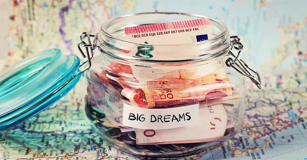 Glass jar labeled 'Big Dreams' filled with euro banknotes, placed on a map.