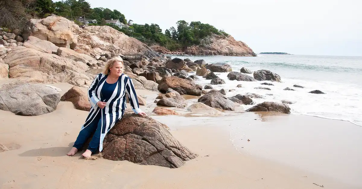 Kim Woods sitting on a rock at the beach, looking out at the ocean.