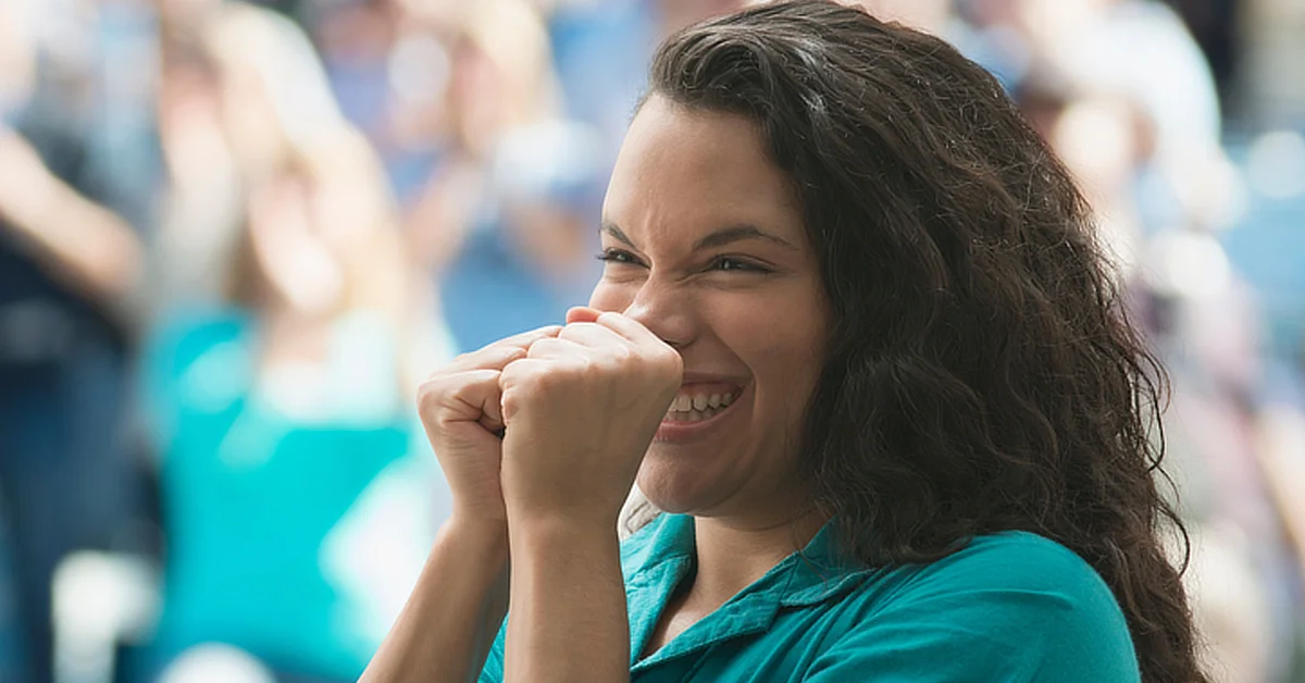 Person expressing excitement or anticipation, clenching their fists and smiling, with a blurred crowd in the background.