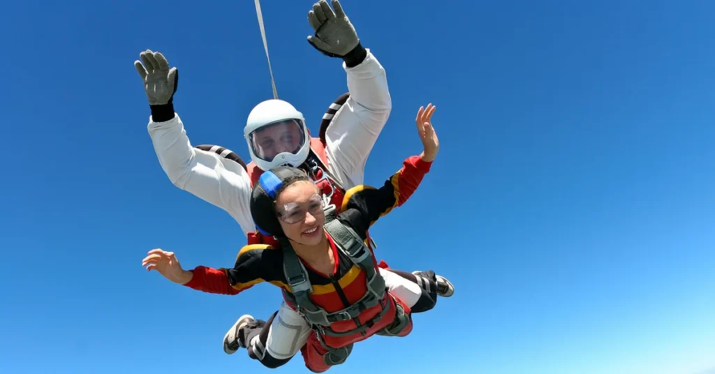 Two people tandem skydiving, with the instructor behind and the student in front, freefalling through a clear blue sky.