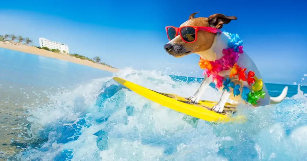 Small dog wearing sunglasses and a colorful lei, riding a wave on a yellow surfboard at the beach, with clear blue skies and distant palm trees in the background.