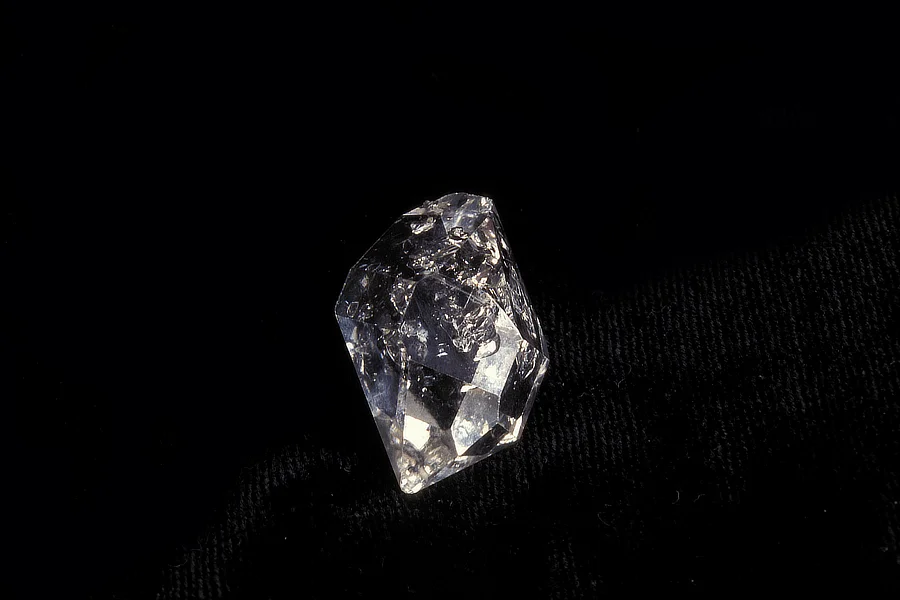 Close-up of a rough, uncut Herkimer diamond resting on a black surface.