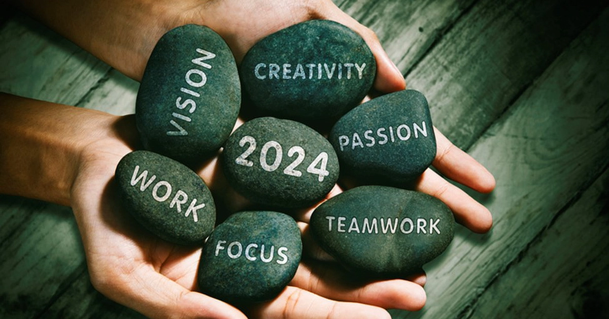 Hands holding several smooth stones, each engraved with words like 'vision,' 'creativity,' '2024,' 'passion,' 'work,' 'focus,' and 'teamwork.'