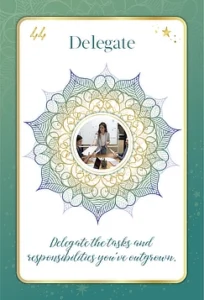 Oracle card titled 'Delegate' with the number 44 at the top. It features a mandala design with a central photo of a woman in a professional setting, sitting at a desk, discussing with colleagues. The card reads, 'Delegate the tasks and responsibilities you've outgrown.'