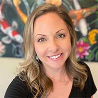 Client testimonial image featuring Emily Aarons with wavy blonde hair, wearing a black top, smiling in front of a colorful koi fish painting.