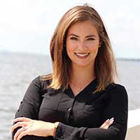 Client testimonial image of Janelle Lara in a black blouse, smiling with a waterfront background.