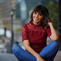 Client testimonial image featuring Marisa Corcoran in a red lace top and jeans, smiling while sitting outdoors in an urban setting.