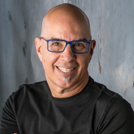 Rob Actis, a bald man with glasses, a goatee, and a black shirt, smiling against a neutral background.