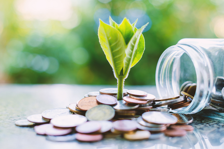 Plant growing from coins outside the glass jar on blurred green natural background for business and financial growth concept