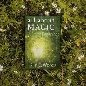 A copy of "All About Magic: Beginnings" by Kim E. Woods placed in a field of wildflowers.