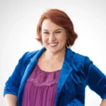 Candy Barone smiles confidently, wearing a vibrant blue velvet blazer over a purple top. She stands with her hands on her hips against a plain white background.