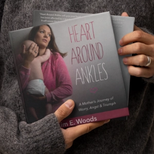 A person holding multiple copies of "Heart Around Ankles: A Mother’s Journey of Worry, Angst & Triumph" by Kim E. Woods.