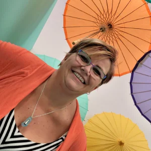 Jackie Barker standing under colorful umbrellas, including orange, purple, and yellow.