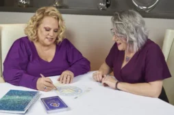 Kim Woods and 1:1 client sitting at a table, reviewing astrological charts and notes together.