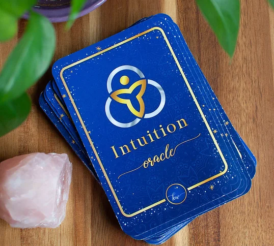 Kim Woods' Intuition Oracle Cards with gold detailing, placed on a wooden surface next to a Rose Quartz crystal.