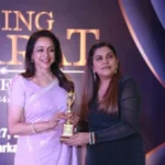 Vandana Tolani receives an award on stage, standing with another woman, both holding a trophy and smiling at the camera.