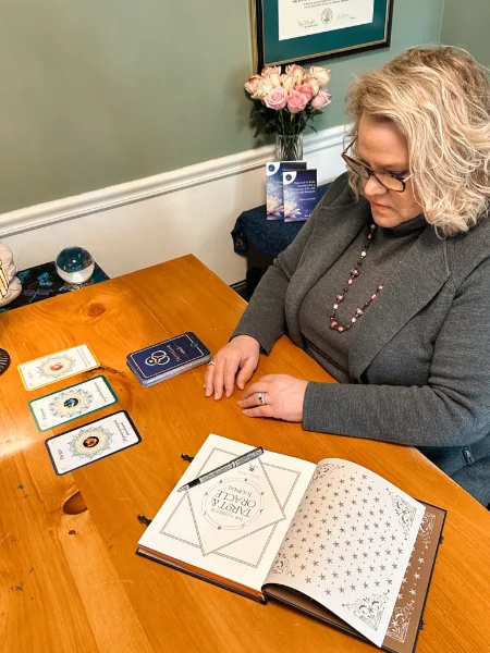 Kim Woods sitting at a desk with an open book, a stack of books, and working on the astrological forecast