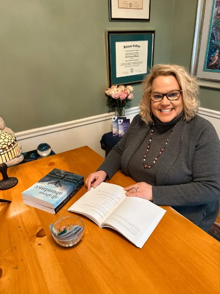 Kim Woods sitting at a desk, looking at tarot cards and an open journal, working on the annual Astrological Forecast.