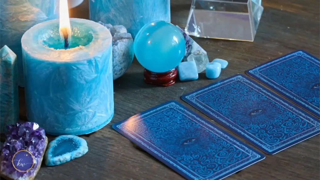 Blue candles, tarot cards, a crystal ball, and healing crystals arranged on a wooden table, creating a spiritual and calming setting. The scene symbolizes introspection and overcoming a lack mindset through self-awareness and clarity.