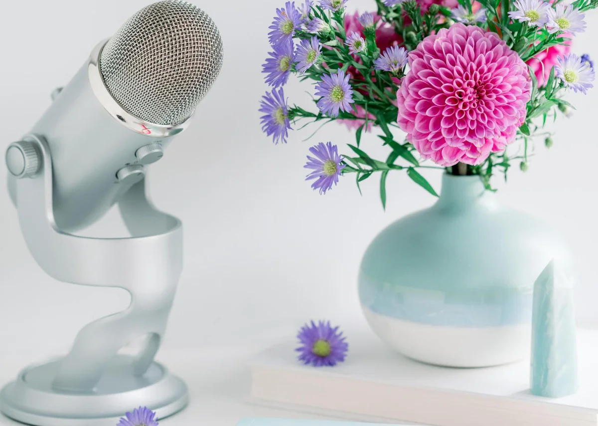 Silver podcast microphone, pastel vase with pink and purple flowers, and a crystal, suggesting a February 2025 astrology forecast.