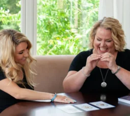 Kim Woods and one of her clients sit at a table, joyfully engaging in a personal success reading with oracle cards, creating an atmosphere of insight, connection, and clarity.