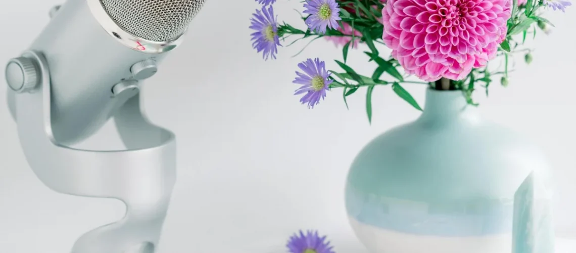 Silver podcast microphone, pastel vase with pink and purple flowers, and a crystal, suggesting a February 2025 astrology forecast.