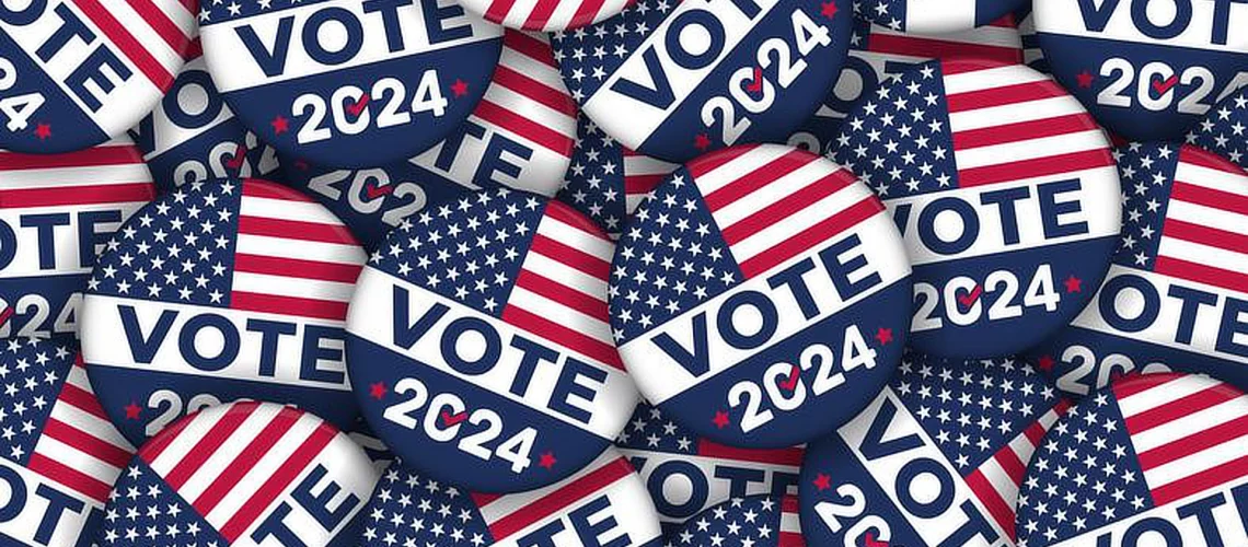 A collection of round "Vote 2024" buttons featuring the American flag design. The buttons have the word "VOTE" in bold white letters and "2024" below, with a red check mark inside the "0" in "2024." The buttons are stacked and scattered, creating a visually layered pattern