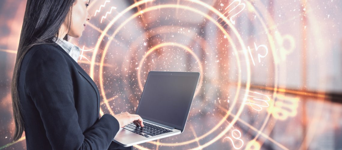 Attractive young european businesswoman with laptop and abstract zodiac sign hologram on blurry office interior background. Technology and astrology concept. Double exposure